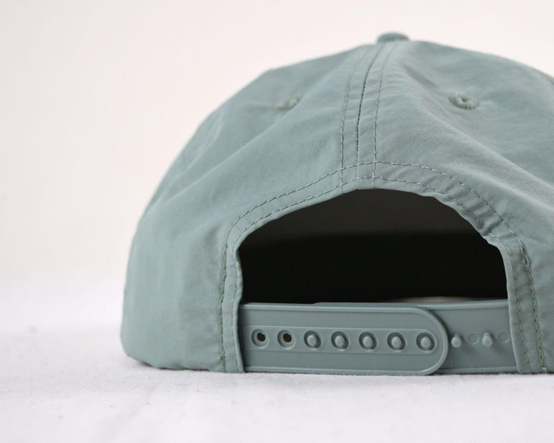 May include: A pale teal baseball cap with a curved peak and adjustable strap. The cap has a classic six-panel design with stitched seams and a plastic snap closure for a custom fit. The hat is made of a lightweight, durable material.