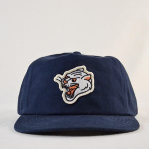 May include: A navy blue baseball cap with a white and orange embroidered panther head on the front.