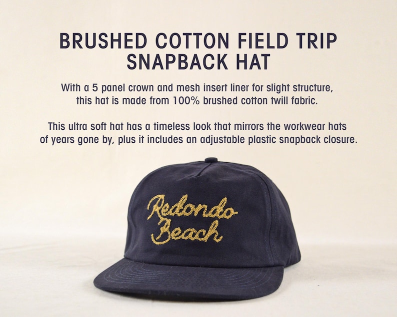 Puede incluir: Gorra snapback azul marino con bordado dorado "Redondo Beach". Cuenta con una visera curva y cierre de broche de pl&aacute;stico ajustable. El texto "BRUSHED COTTON FIELD TRIP SNAPBACK HAT" est&aacute; en la parte superior.