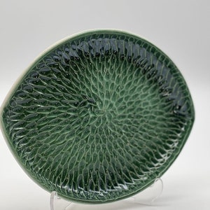 Puede incluir: Un plato de servir de cerámica verde con un diseño texturizado en relieve que se asemeja a escamas. El plato tiene forma ovalada y un borde blanco.