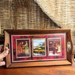 May include: A wooden serving tray with a red and black tartan design. The tray features three images: a couple in traditional Scottish clothing, a scenic landscape, and a group of people in a pub. The text "Joseph Walker" is printed on the tray.