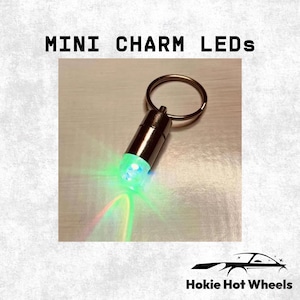 May include: A cylindrical metal keychain charm with a built-in LED light emitting a bright green glow. The device features a circular metal ring at the top for attachment. The text MINI CHARM LEDs and Hokie Hot Wheels appear in the image.