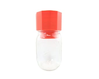 Op de afbeelding: Een rode achthoekige deksel voor een glazen pot. De deksel is gemaakt van plastic en heeft een glad oppervlak. De pot is van helder glas en heeft een getextureerd oppervlak.
