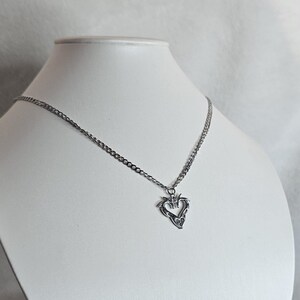 May include: A silver chain necklace with a heart-shaped pendant. The pendant is detailed with intricate designs.