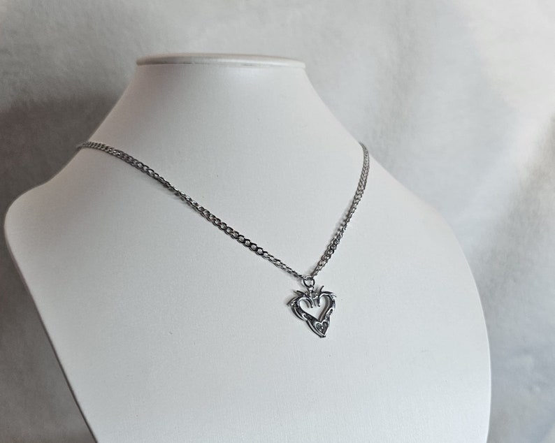 May include: A silver chain necklace with a heart-shaped pendant. The pendant is detailed with intricate designs.