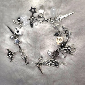 Może przedstawiać: Srebrna bransoletka z różnymi zawieszkami, w tym czaszką, pająkiem, gwiazdą, sercem, mieczem i kartą do gry. Zawieszki są przymocowane do srebrnego łańcuszka.