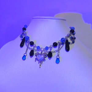 May include: A silver chain necklace with blue and black beads, a silver heart charm, and dangling blue and black beads.