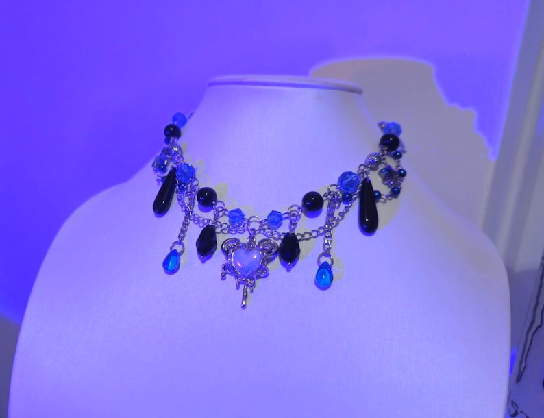 May include: A silver chain necklace with blue and black beads, a silver heart charm, and dangling blue and black beads.