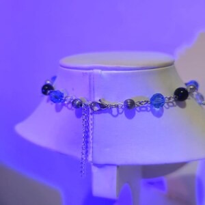 May include: A silver chain necklace with blue and black beads on a white mannequin bust. The necklace has a silver clasp.