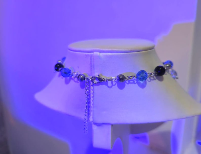 May include: A silver chain necklace with blue and black beads on a white mannequin bust. The necklace has a silver clasp.
