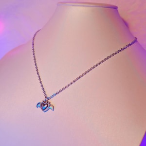 May include: A silver chain necklace with a heart pendant featuring small wings. The heart is silver with a slightly iridescent finish.