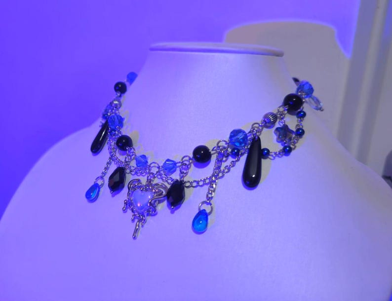 May include: A silver chain necklace with black and blue beads, a silver charm, and dangling blue and black teardrop-shaped beads.
