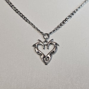 May include: A silver chain necklace with a silver pendant in the shape of a stylized heart.