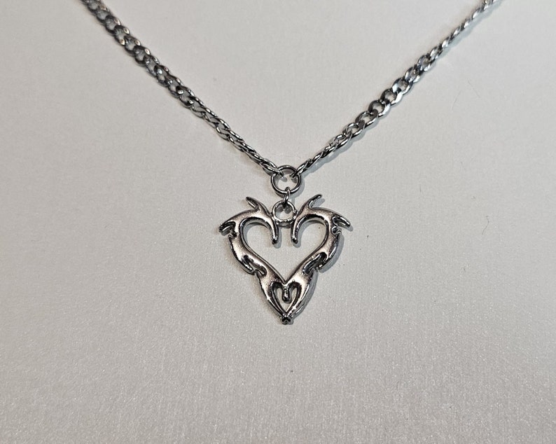 May include: A silver chain necklace with a silver pendant in the shape of a stylized heart.