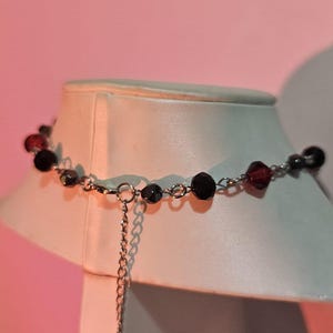 May include: A silver chain necklace with black and red beads. The necklace has a delicate chain and is adjustable in length.