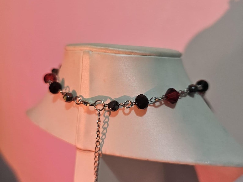 May include: A silver chain necklace with black and red beads. The necklace has a delicate chain and is adjustable in length.