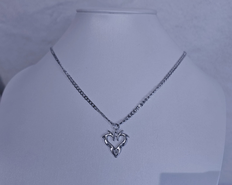 May include: A silver chain necklace with a silver pendant in the shape of a stylized heart.