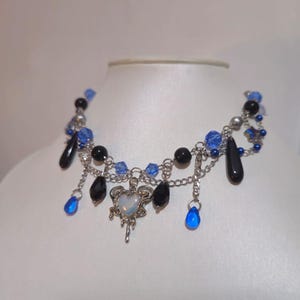 May include: A silver necklace with blue and black beads, a silver heart charm, and dangling teardrop-shaped blue beads.