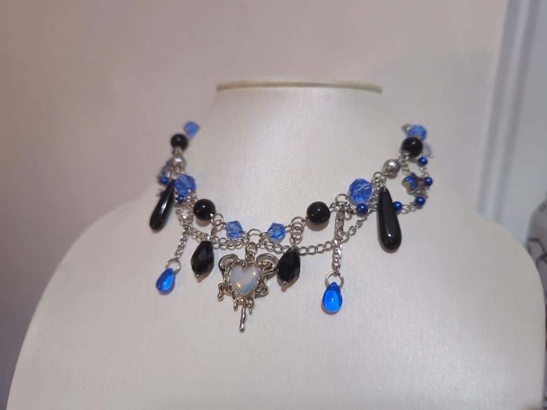 May include: A silver necklace with blue and black beads, a silver heart charm, and dangling teardrop-shaped blue beads.
