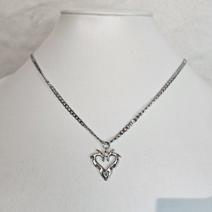 May include: A silver chain necklace with a heart-shaped pendant. The pendant is made of silver and has a detailed design.