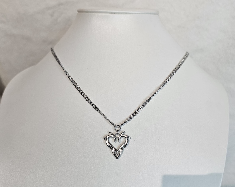 May include: A silver chain necklace with a heart-shaped pendant. The pendant is made of silver and has a detailed design.