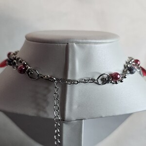 May include: A silver chain necklace with pink and white beads and a silver clasp. The necklace is on a white mannequin.