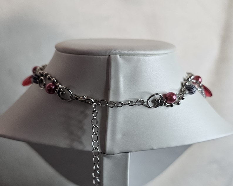 May include: A silver chain necklace with pink and white beads and a silver clasp. The necklace is on a white mannequin.