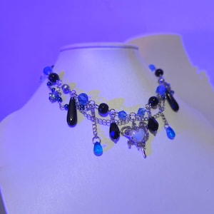 May include: A silver chain necklace with black and blue beads, a silver heart charm, and dangling blue teardrop-shaped crystals.