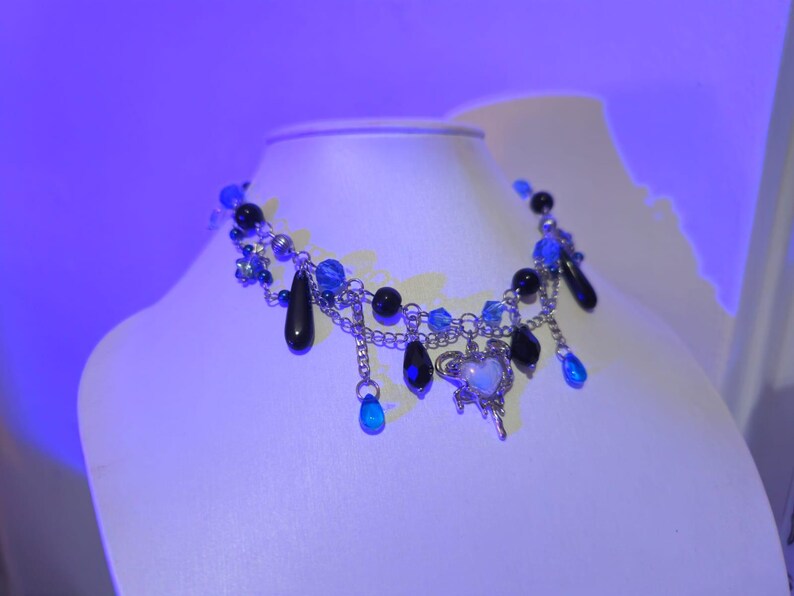 May include: A silver chain necklace with black and blue beads, a silver heart charm, and dangling blue teardrop-shaped crystals.