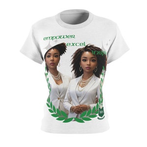 May include: White t-shirt with a green laurel wreath design and two women in white suits. The text "empower excel inspire" is printed on the shirt.