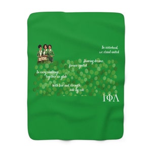 Op de afbeelding: Een heldergroene deken met een illustratie van drie vrouwen in groene outfits en tekst. De tekst bevat zinnen als "In zusterschap, staan we verenigd" en "Dromen delen, voor altijd ontstoken". De deken heeft een zachte, pluche textuur.