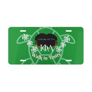 Pode incluir: Placa de matrícula verde com detalhes brancos e o texto "Walk in Unity". O design inclui um contorno de tartaruga, tartarugas e as letras gregas IΦA. A frase "Leadership and Love" também está presente.