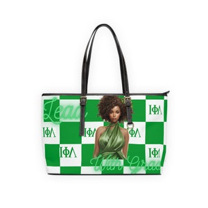 May include: A green and white chequered tote bag with a black leather handle and trim. The bag features a graphic of a woman with an afro and the text "Lead With Grace" and "IΦΛ".