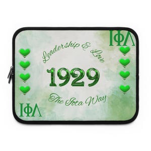 Op de afbeelding: Een zwarte laptoptas met een groen en wit ontwerp. Het ontwerp bevat de woorden "Leadership & Love", het nummer "1929" en de tekst "The Iota Way". Groene harten en Griekse letters zijn ook aanwezig.