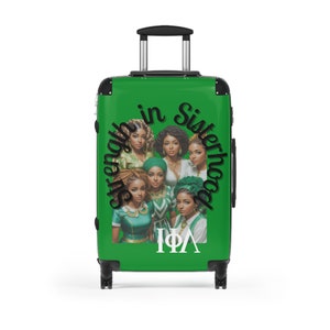Op de afbeelding: Groene rolkoffer met een afbeelding van zeven vrouwen, de tekst "Strength in Sisterhood" en "IΦA". De koffer heeft een uitschuifbare handgreep en zwarte wielen.