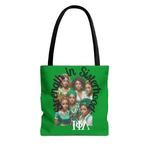 Op de afbeelding: Groene draagtas met zwarte handvatten. De tas toont een afbeelding van zes vrouwen met de tekst "Strength in Sisterhood" en de Griekse letters "ΙΦΛ". De vrouwen dragen verschillende outfits en hoofdbedekkingen.