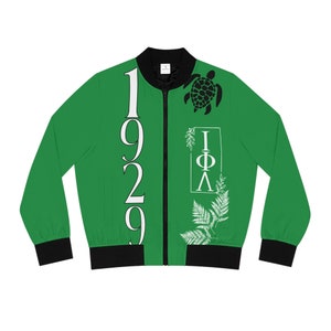 Peut inclure: Une veste bomber verte avec une fermeture éclair noire et des poignets et une ceinture côtelés noirs. La veste présente un motif blanc sur le devant avec le texte "1929" et "IΦΛ" avec une fougère blanche et un motif de tortue noire.