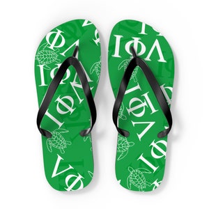 Pode incluir: Um par de chinelos verdes com tiras pretas. Os chinelos têm um padrão branco de letras gregas e tartarugas marinhas.