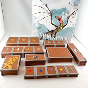 Könnte beinhalten: Ein Brettspiel namens "Wyrmspan" mit einer Schachtel, die einen Drachen mit weißen Flügeln vor einem blauen Hintergrund zeigt. Das Spiel enthält Holzkisten mit verschiedenen Symbolen und eine Holzbasis.