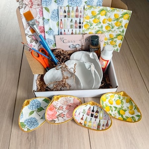 Puede incluir: Un kit de manualidades con una variedad de suministros, que incluyen pinceles, tijeras y Mod Podge. El kit incluye varios platos decorativos con diseños florales, de limón y de botellas de vino. El kit está empaquetado en una caja de cartón.