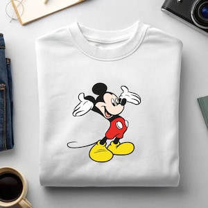 May include: White sweatshirt featuring a colorful graphic of Mickey Mouse. The cartoon character is depicted with black ears, a black head, white gloves, red shorts, and yellow shoes. The sweatshirt is a crew neck style.