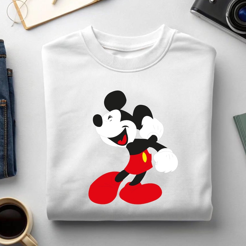 May include: White crewneck sweatshirt featuring a smiling Mickey Mouse graphic. The cartoon character is depicted in his classic outfit: red shorts, yellow buttons, black body, and white gloves. The sweatshirt is made of a soft, comfortable material.