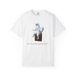 Puede incluir: Camiseta blanca con un meme de un gato blanco y esponjoso sentado en una caja marrón. El gato tiene una expresión de mal humor. El texto "do i look like i give a fuck?" está impreso debajo.