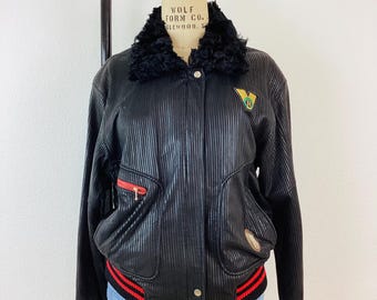 May include: Black leather bomber jacket with a ribbed texture, red and white striped trim, and a faux fur collar. The jacket has a zipper closure and a patch with the text "Wolf Form Co. Glenwood, N.Y." on the left side of the collar.