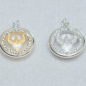 Pode incluir: Dois pingentes de prata com um design de cristal transparente. Um pingente apresenta um Garuda dourado, uma ave mítica, dentro do cristal. O outro pingente apresenta um Garuda prateado dentro do cristal.