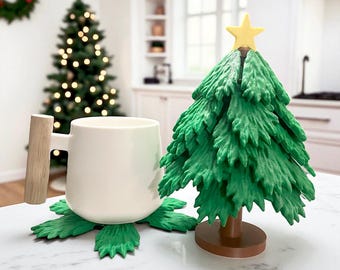 May include: A white mug with a wooden handle rests on a green leaf-shaped coaster. Beside it is a green Christmas tree decoration with a yellow star on top. A decorated Christmas tree is in the background.