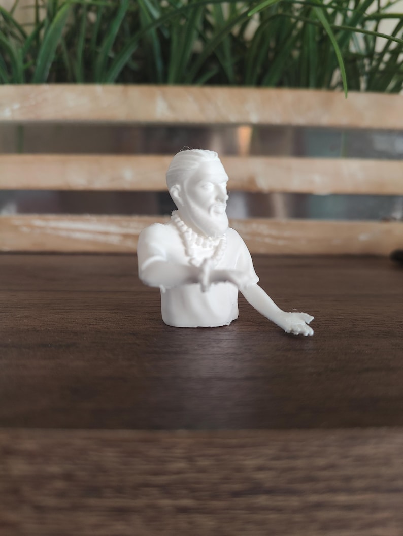 May include: A white 3D printed figurine of a person with a beard and hair tied back, wearing a short-sleeved shirt and a beaded necklace. The figure is depicted from the chest up with one arm extended outwards, showing detailed facial features.