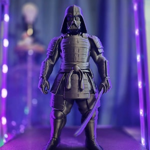 May include: A black action figure of Darth Vader in samurai armor, holding a katana. The figure is in a display case with purple lighting. The figure is approximately 6 inches tall.
