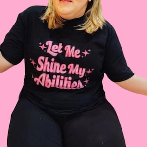 May include: Black t-shirt with pink lettering that reads "Let Me Shine My Abilities".