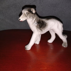 May include: A white porcelain figurine of a grey and black dog standing on a red surface.